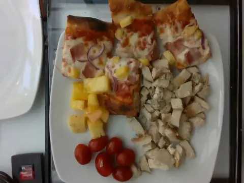 Four pieces of pizza with pineapple, diced chicken and cherry tomatoes on a white plate.